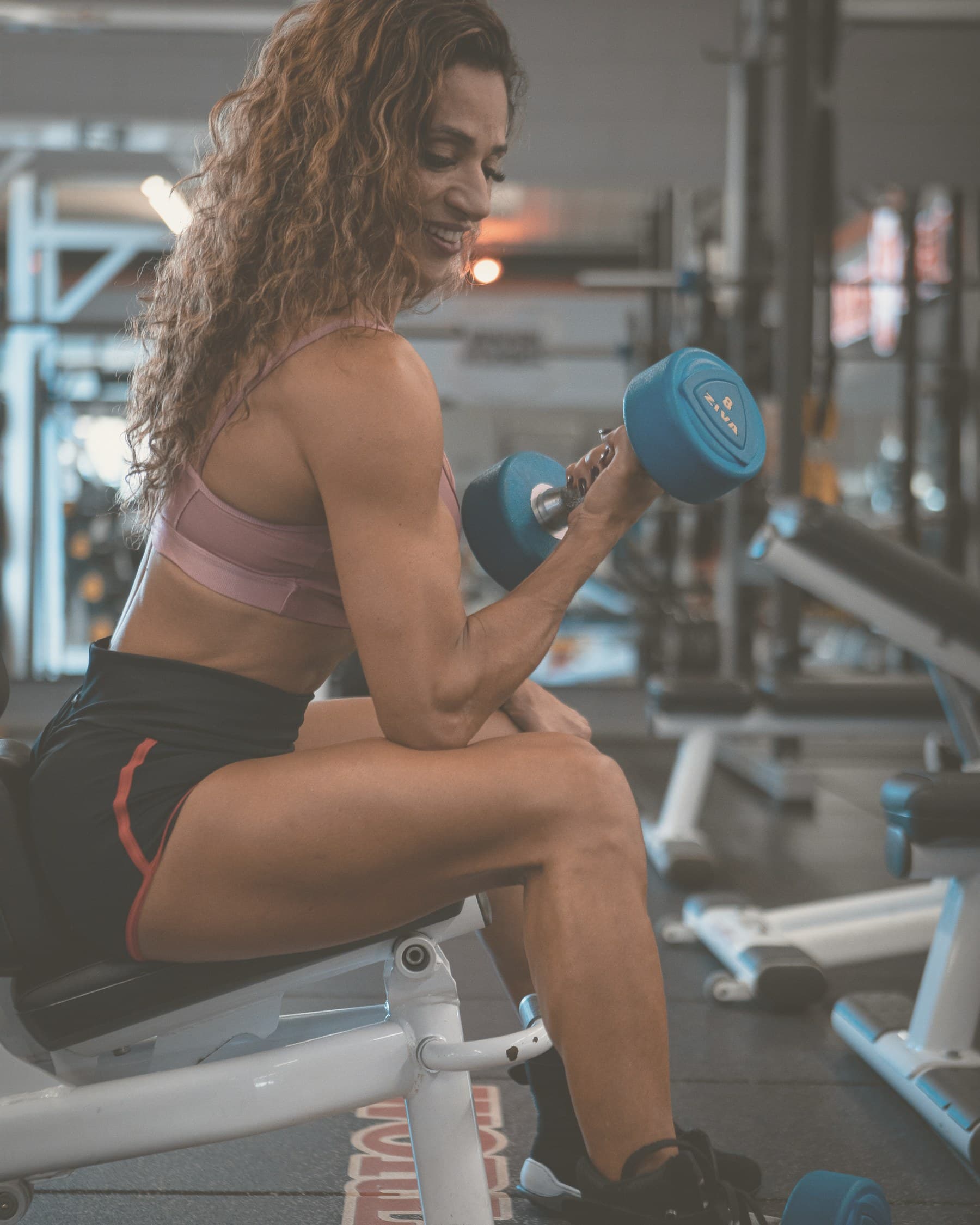 Neide Ferreira sentada no banco, rosca com halter.